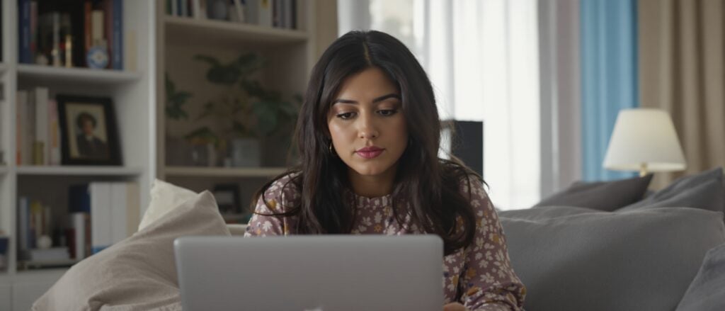Young woman focused on laptop, working on dissertation in cozy living room, emphasizing personalized academic support and research development.