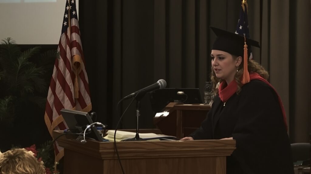 Graduate student presenting during dissertation defense with American flags in the background, illustrating the pressure of academic evaluation.